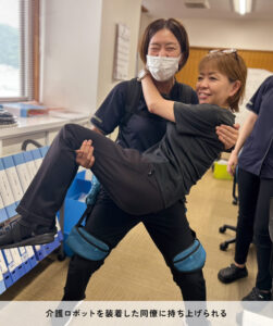 介護ロボットを装着した同僚に持ち上げられる武田さん